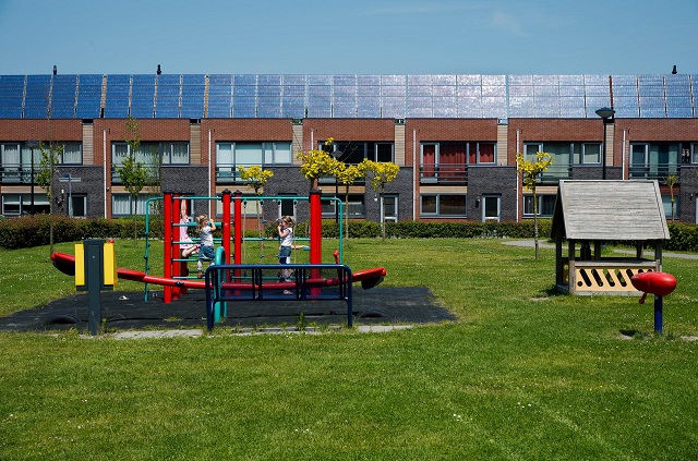 Rij huizen met zonnepanelen met op de voorgrond een speelplaats met kinderen